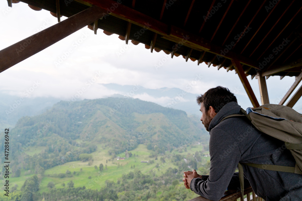 Horizontal portrait of latin american man in Salento viewpoint with mountains in background. Horizontal view of man sightseeing at sunset with backpack. People and travel destination in Colombia Horizontal portrait of latin american man in Salento viewpoint with mountains in background. Horizontal view of man sightseeing at sunset with backpack. People and travel destination in Colombia