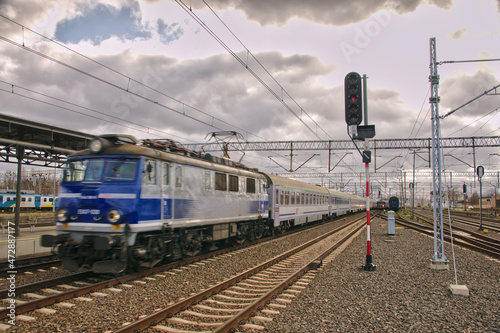 Pociąg osobowy pośpieszny składający się z lokomotywy elektrycznej jadący z zauważalną szybkością, który mija semafor przy peronach. photo