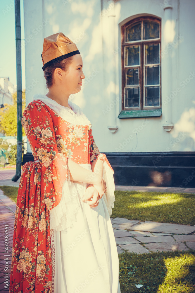 Portrait of brunette woman dressed in red historical Baroque clothes with old fashion hairstyle, outdoors. Middle class medieval dress Portrait of brunette woman dressed in red historical Baroque clothes with old fashion hairstyle, outdoors. Middle class medieval dress