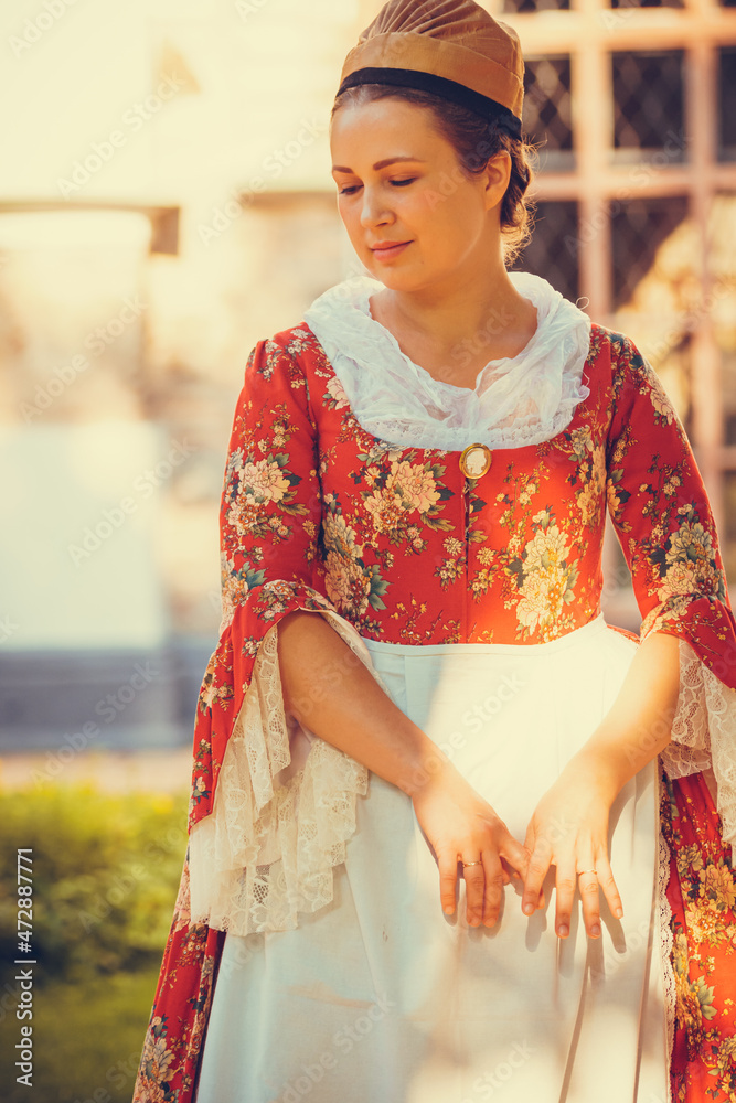 Portrait of brunette woman dressed in red historical Baroque clothes with old fashion hairstyle, outdoors. Middle class medieval dress