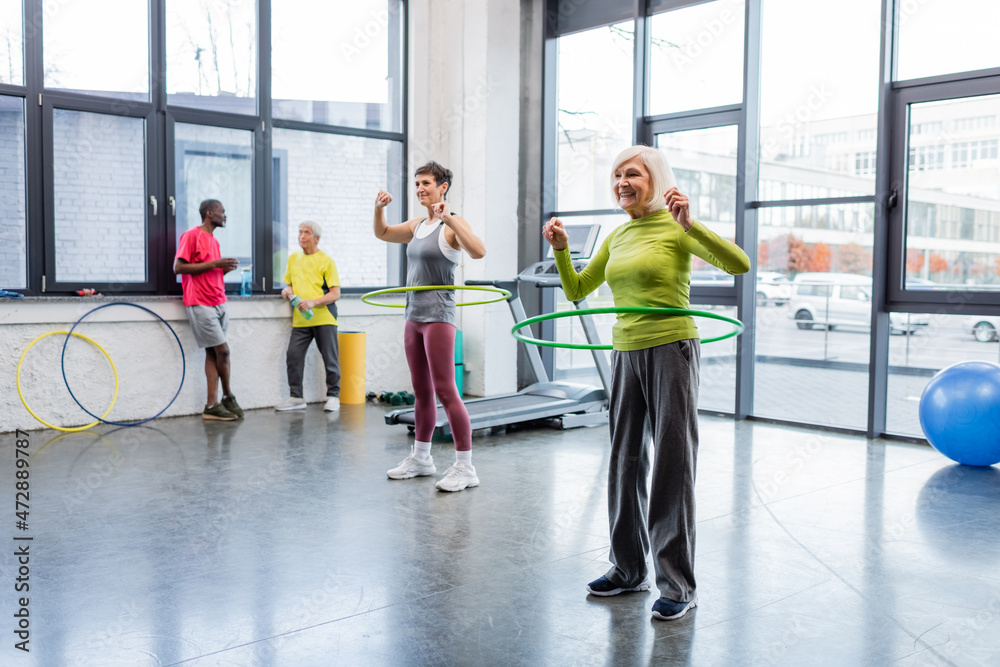 Fototapeta premium Happy elderly woman exercising with hula hoop on sports center.