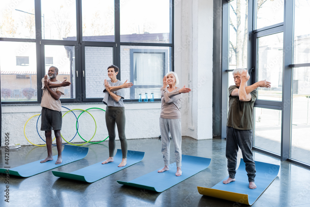 Multicultural senior people practicing yoga on mats in sports center. Multicultural senior people practicing yoga on mats in sports center.