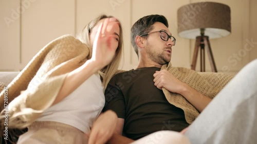 Young couple watching a scary movie on TV looking at camera with scared faces holding plead sitting on the sofa in the apartment. High quality 4k footage