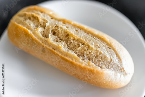 Macro closeup of small Petit Pain french roll in shape of baguette bread loaf fresh baked crust on white plate
