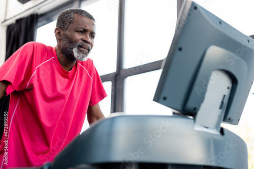 Focused african american sportsman training on blurred treadmill in gym.