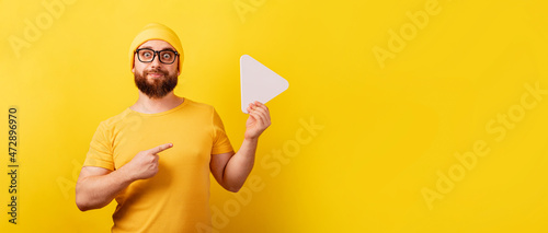 man pointing at play button sign over yellow background, technology, media player button, panoramic layout