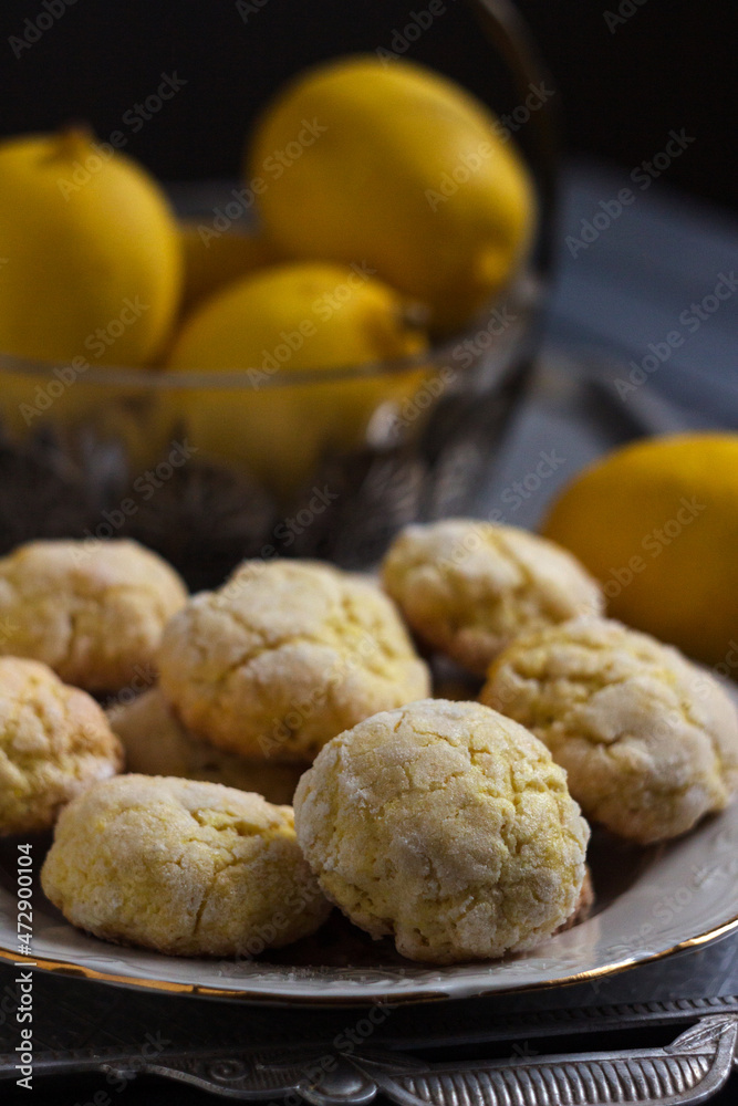 Round lemon cookies on a white plate surrounded by lemons fruit, gray wooden background. Homemade cookies Round lemon cookies on a white plate surrounded by lemons fruit, gray wooden background. Homemade cookies