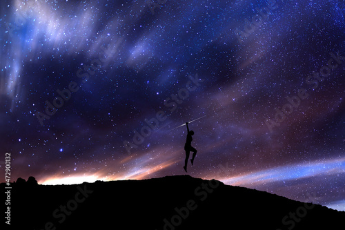 Girl silhouette jumping above the hill in the starry night. Bright milky way galaxy behind her.