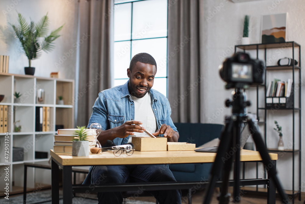 African american blogger unboxing new smartphone and recording video on camera. Young guy sharing with subscribers his feedback about modern gadget. African american blogger unboxing new smartphone and recording video on camera. Young guy sharing with subscribers his feedback about modern gadget.