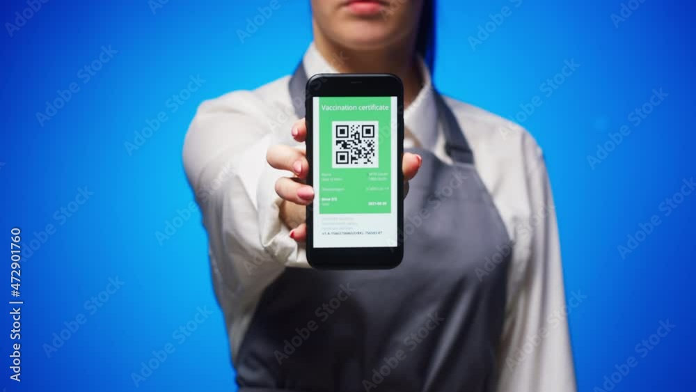 Woman worker showing on phone vaccination passport with qr code on blue background, international coronavirus covid 19 vaccine certificate on mobile device, green zone. Woman worker showing on phone vaccination passport with qr code on blue background, international coronavirus covid 19 vaccine certificate on mobile device, green zone.