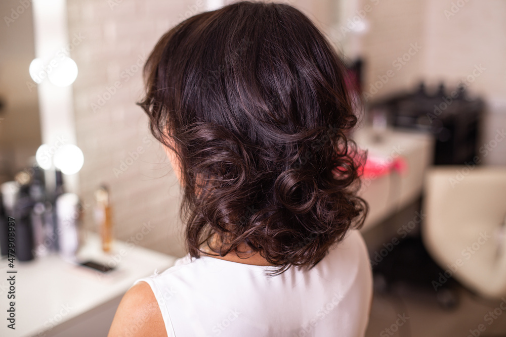 Fototapeta premium Female back with short curly brunette hair in hairdressing salon