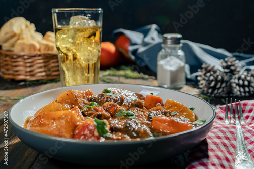 Normal view of a wooden table with a plate of meat stew with potatoes. Space for text. Horizontal orientation.