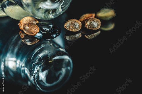 Macro View of Medical Cannabis Seeds with Drops of Oil CBD THC on Black Mirroring Background.