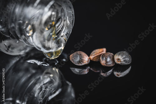 Macro View of Medical Cannabis Seeds with Drops of Oil CBD THC on Black Mirroring Background.