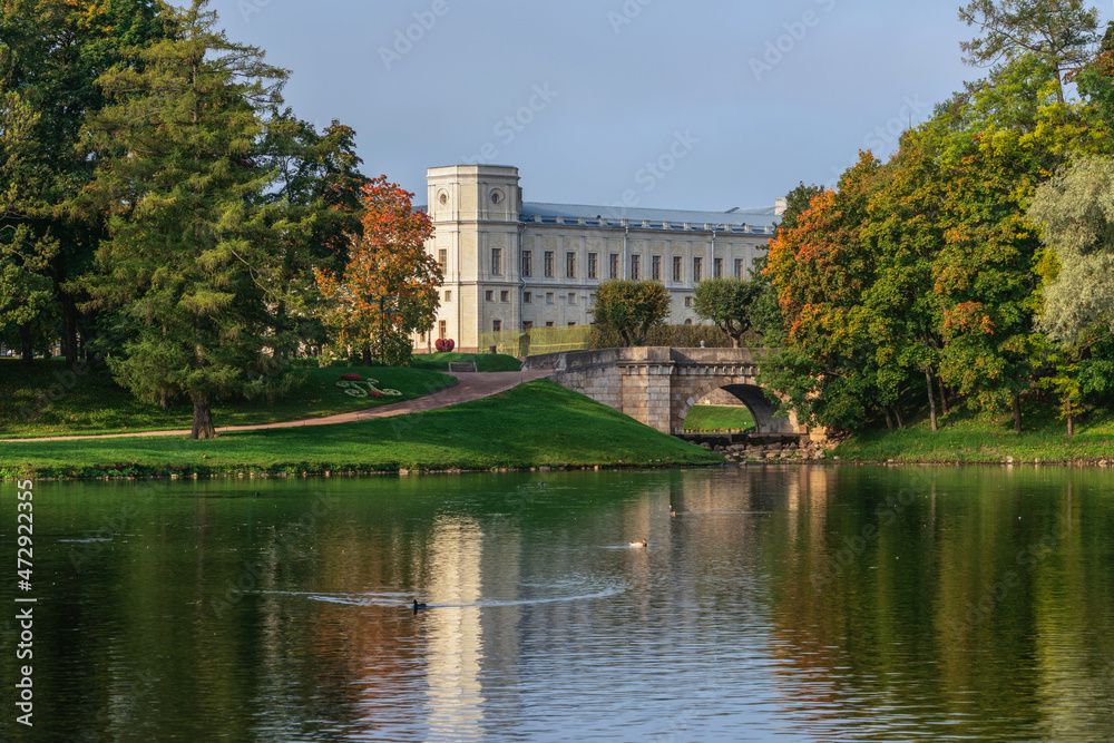 View of the Karpin Bridge over the cascade between the Karpin Pond and the White Lake of Gatchina Park and the Gatchina Palace in the background on a sunny autumn day, Gatchina, St. Petersburg Russia