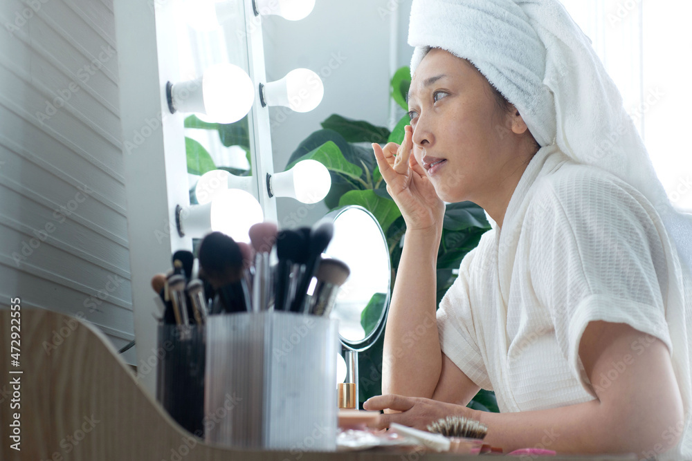 Beautiful girl in bathrobe and turban towel on her head smiles to herself in the mirror, women lifestyle Beautiful girl in bathrobe and turban towel on her head smiles to herself in the mirror, women lifestyle