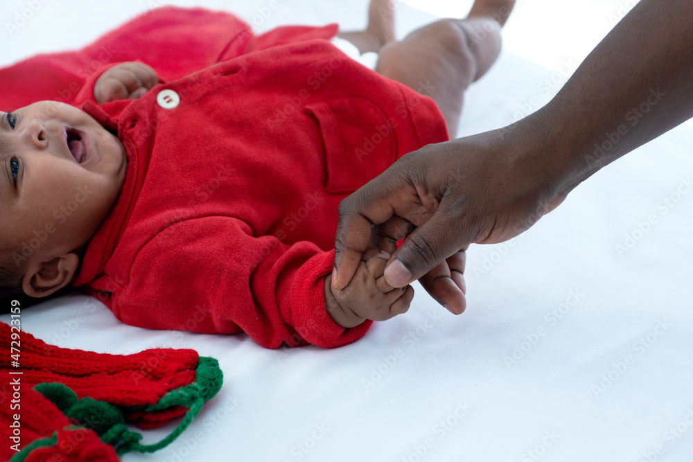 African father holding baby's hand, baby wear Christmas clothes lying on bed at home for celebrate merry Christmas and happy new year, relationship between father and daughter