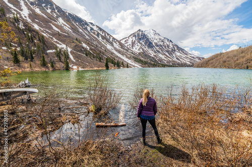 Hiker standing beside a pristine lake in northern Canada with a stunning snow capped mountain background landscape. Tourism, travel shot in Yukon Territory. 