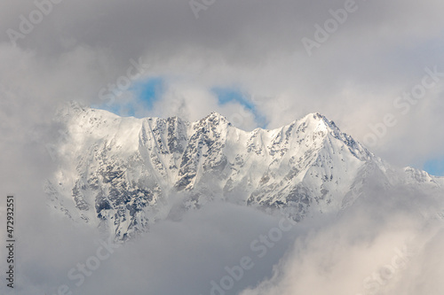 Snowy covered mountain top on winter with misty, cloud covered snow, high altitude peak. Landscape, stunning nature background. 