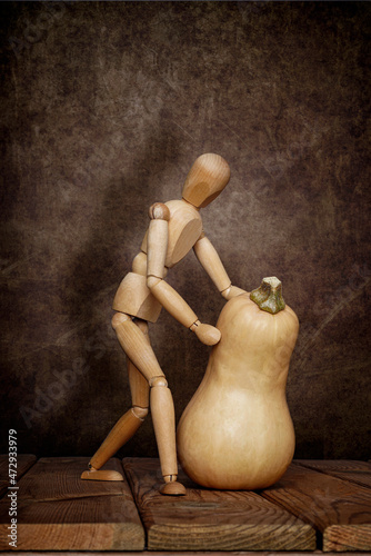 A wooden emotional gestalt man with a pumpkin and a scoop on a wooden table and an artistic background. Halloween. photo