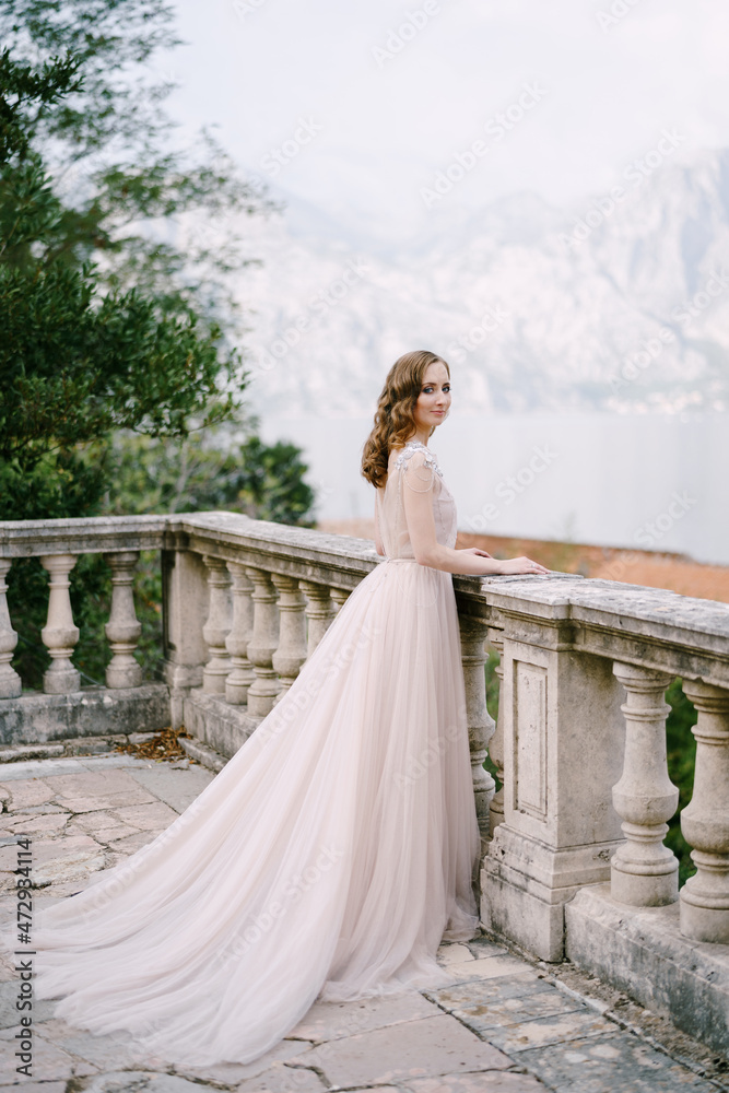 Bride stands on a stone terrace leaning on a balustrade