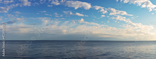 A beautiful panoramic view of the endless sea space and the blue sky with light white clouds in the sunset light. Natural water blue background. Seascape of Crimea