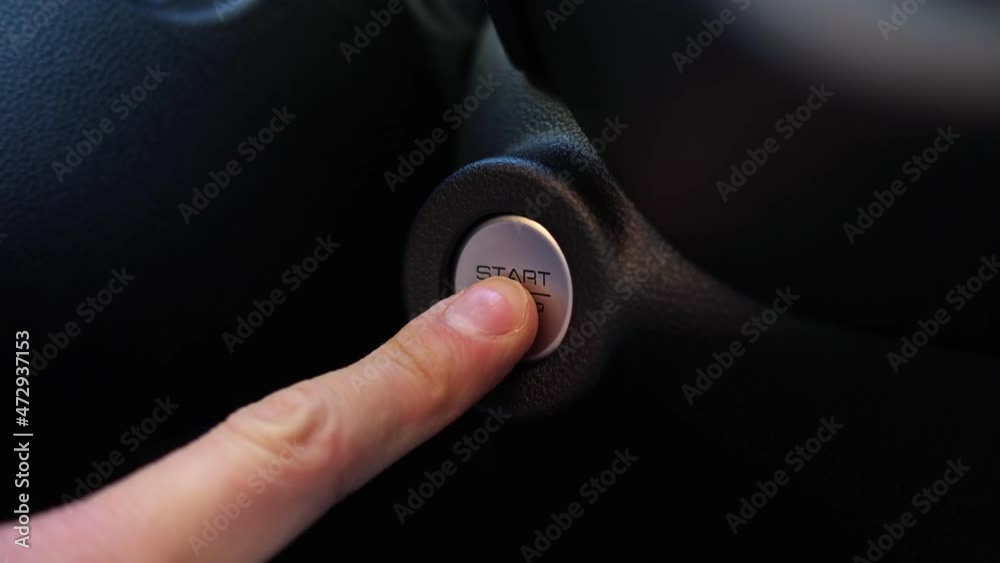 Man uses finger with nail cut unevenly to press start-stop silver-colored button on black plastic dashboard of expensive foreign car closeup