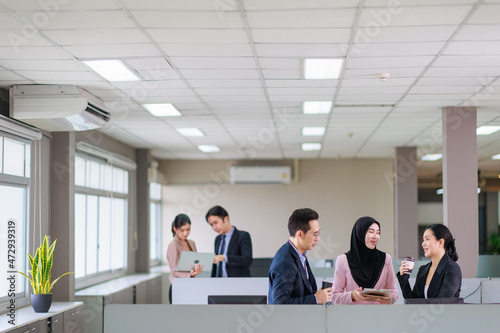Asian officer talking with their coworker in the office while having a coffee break.