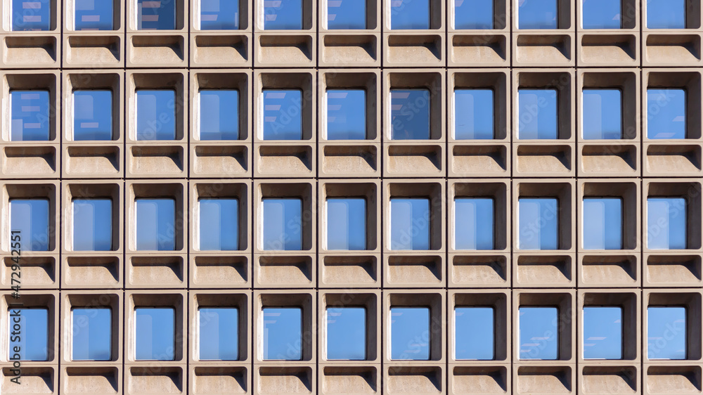 Concrete facade of office building with regular pattern of windows reflecting blue sky Concrete facade of office building with regular pattern of windows reflecting blue sky