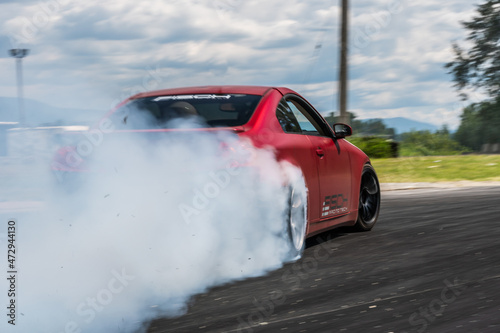 Red Drift Car / Race car drifting around corner very fast with lots of smoke from burning tires on speedway / racetrack / drift track. Infiniti g35 v8. JDM car. Luxury red sport car.