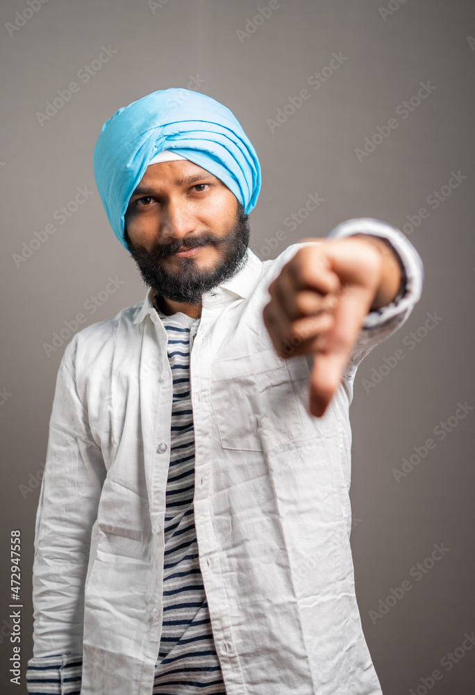 Portrait shot of disappionted indian sikh man showing thumbs down or dislike gesture by looking at camera - concept of bad customer support or rating and negative expression