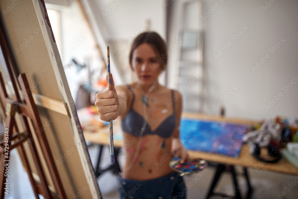 A young sexy and attractive female artist in a bra is standing in front of the easel in her studio and measuring proportions while working on her new painting. Art, painting, studio A young sexy and attractive female artist in a bra is standing in front of the easel in her studio and measuring proportions while working on her new painting. Art, painting, studio