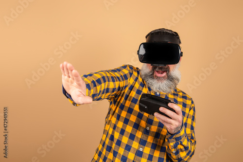 Surprised man in casual shirt posing isolated on yellow background in studio. People lifestyle concept.Watching with virtual reality glasses, playing with joystick © jcalvera