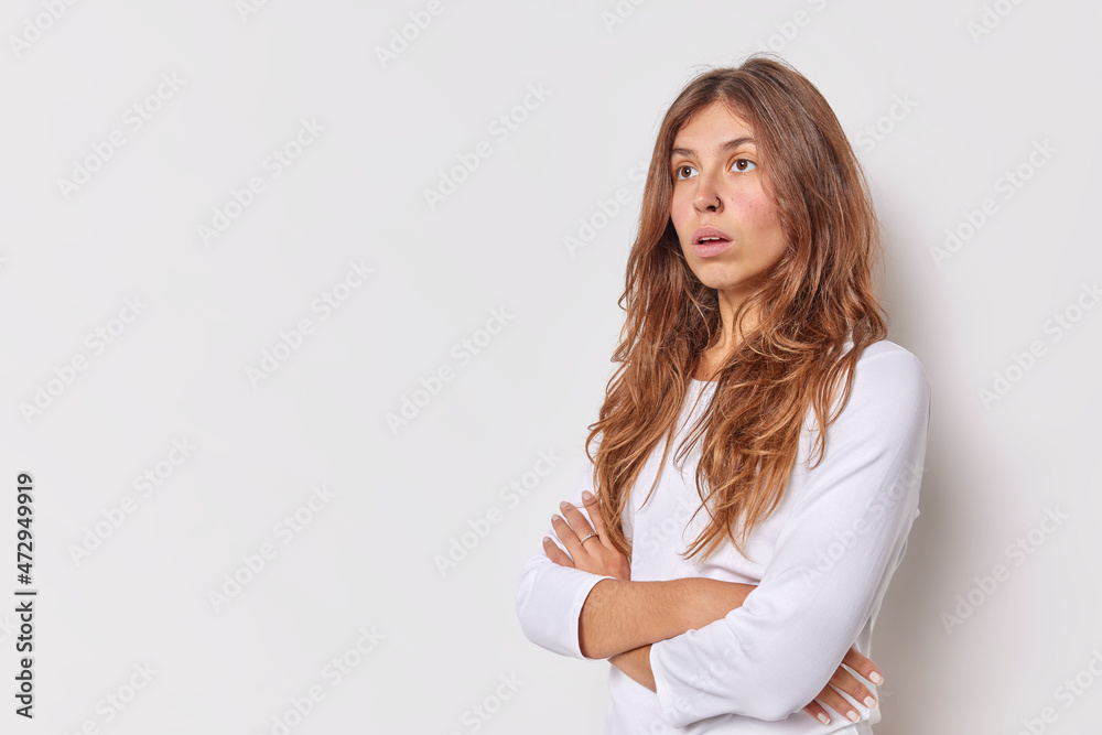 Photo of thoughtful long haired woman has surprised expression keeps arms folded concentrated somewhere with worried look poses against white backgrond with blank space for your promotion or text Photo of thoughtful long haired woman has surprised expression keeps arms folded concentrated somewhere with worried look poses against white backgrond with blank space for your promotion or text