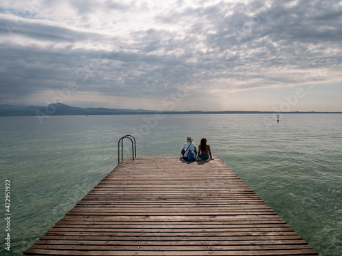 Tourists Sitting on jetty on Lake Garda in Sirmione