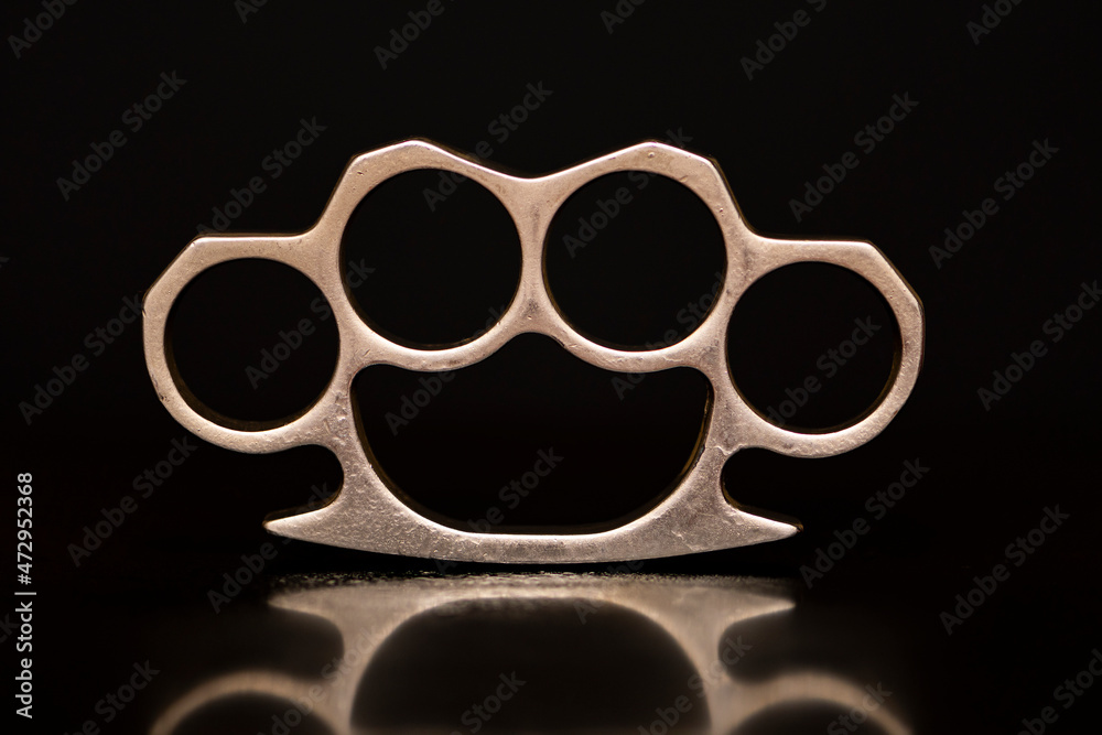 Steel brass knuckles on a black background with reflections. Concept:  hooligan fight, fighting without rules, street banditry, injuries. Stock  Photo