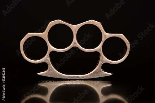 Steel brass knuckles on a black background with reflections. Concept: hooligan fight, fighting without rules, street banditry, injuries. photo