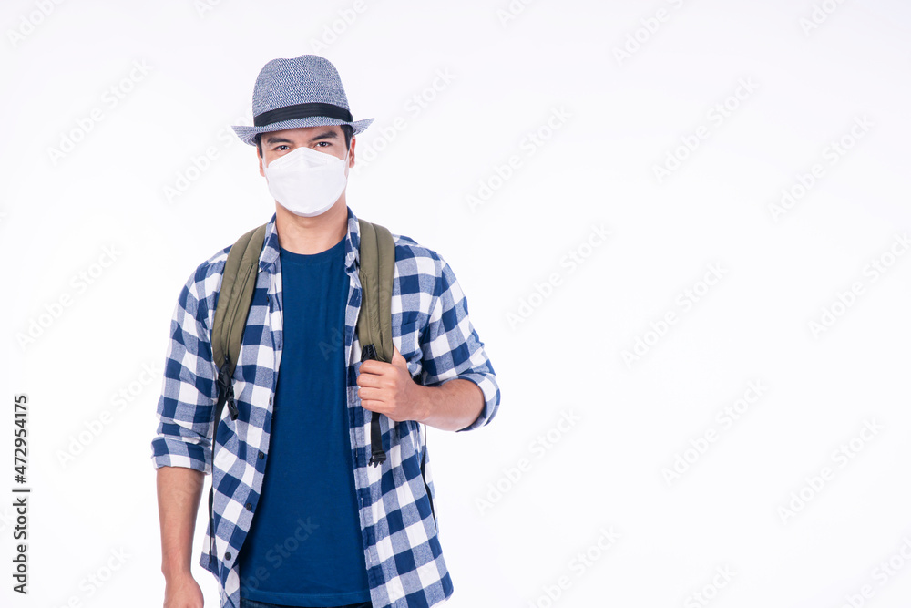 Traveler adventure handsome man wear casual shirt, hat and protective mask safety with backpack standing over isolated white background. New normal lifestyle travel vacation concept. Traveler adventure handsome man wear casual shirt, hat and protective mask safety with backpack standing over isolated white background. New normal lifestyle travel vacation concept.