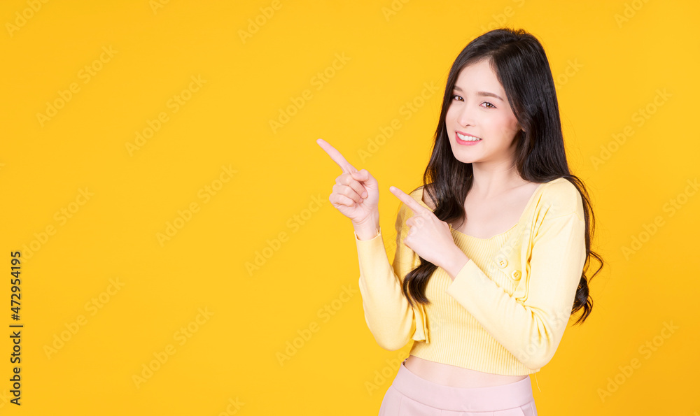 Cheerful asian woman use finger pointing to product or empty copy space while standing over isolated on yellow background. Adverisement presenting concept. Cheerful asian woman use finger pointing to product or empty copy space while standing over isolated on yellow background. Adverisement presenting concept.