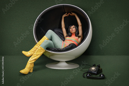 Young woman from the 60s sitting in a vintage ball chair, her rotary dial telephone off the hook at her feet photo