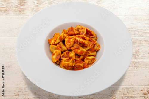 Typical agnolotti del plin, stuffed egg pasta ravioli from Langhe, Piedmont, Italy, seasoned with tomato sauce in white dish on wooden table photo