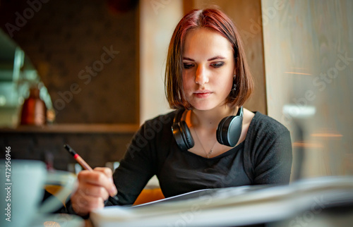 young teenager redhead girl student drawing with pencil in paper album sitting in cafe