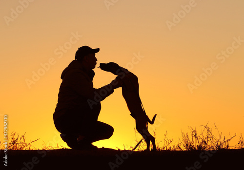 Silhouettes of a man with a small puppy on a sunset background