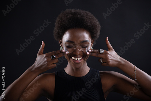 Beautiful smiling young ethnic african american black woman applying moisturizer white cream on her face with emotion like american football player