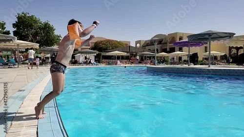 A boy-child dives into the pool water, he jumps from the edge of the pool, creating a lot of splashes of water. summer, holidays, swimming pool, slow motion