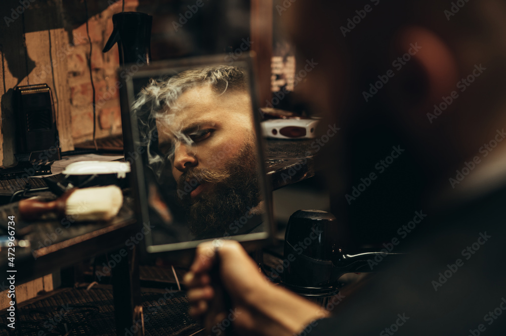 Man looking herself in the mirror while sitting in chair at a barbershop Man looking herself in the mirror while sitting in chair at a barbershop