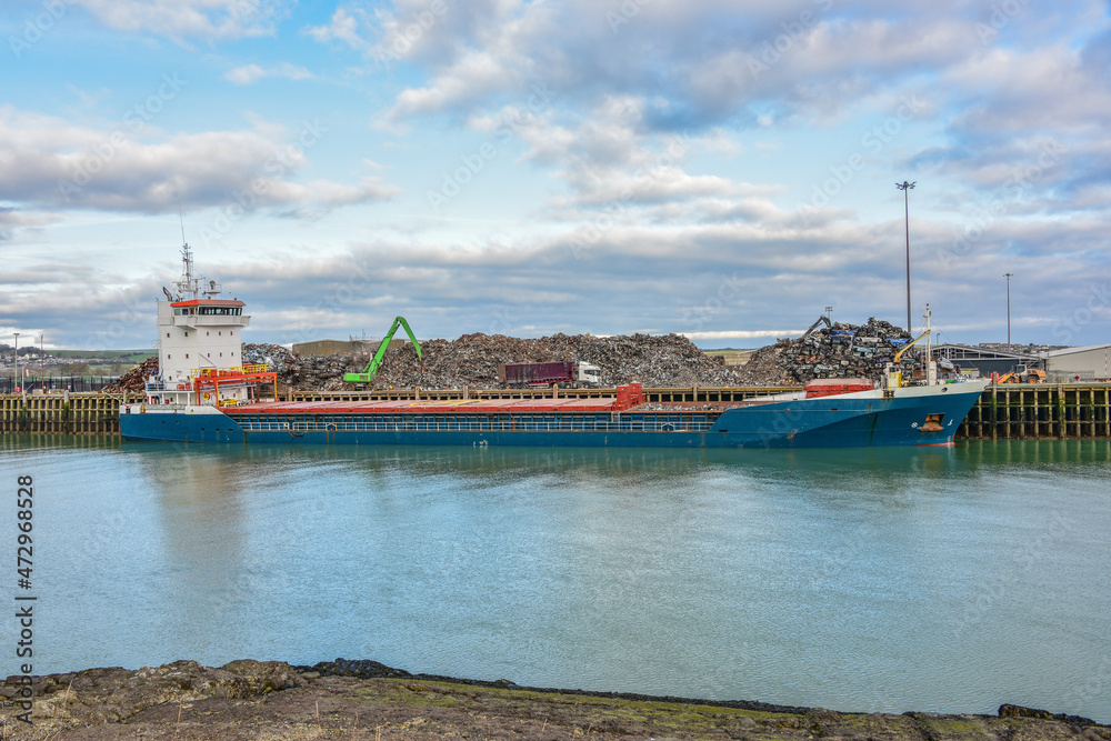 Ship moored in the harbour of Newhaven, UK, being loaded with scrap metal for export, out of the country. Lorry delivering more scrap meatal.