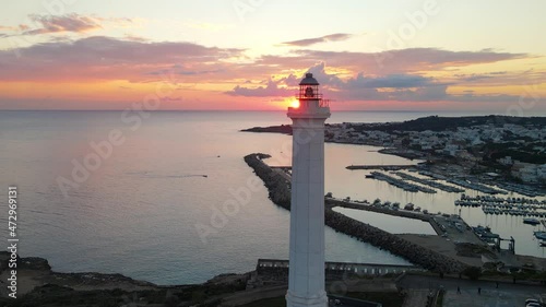 Long Flight around Faro di Santa Maria di Leuca at sunset, with the Port in the background - 4K - Inspiring Aerial Footage - Sun right above the horizon - lighthouse close up and wide view