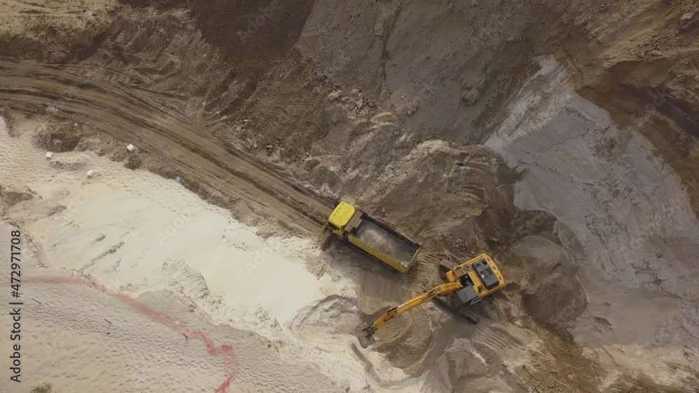 Excavator load the sand into dump truck. Mining truck transport the minerals in the sand quarry. Aerial view of an open pit mining. Excavator load the sand into dump truck. Mining truck transport the minerals in the sand quarry. Aerial view of an open pit mining.