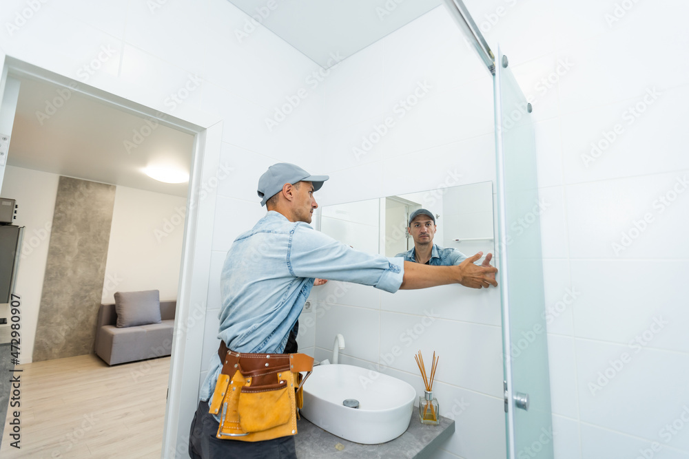 Handyman installing mirror in bathroom.